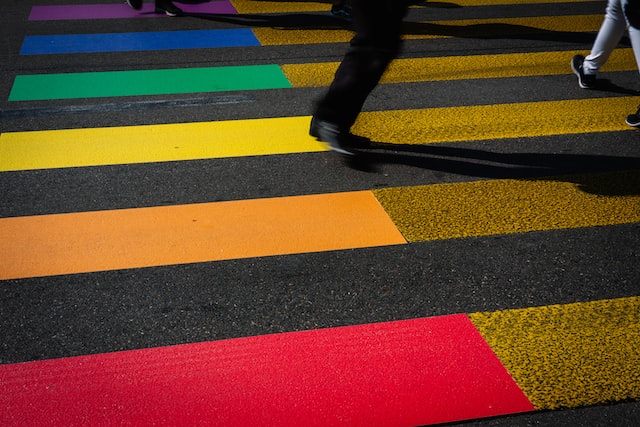Photo of people walking on crosswalk with purple, blue, green, yellow, orange and red stripes. 